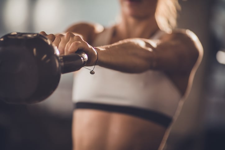 Close-up van een vrouw die een kettlebell swingt in de sportschool