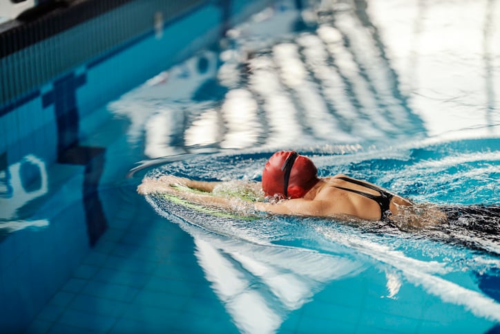 vrouw zwemt in zwembad met badmuts en zwembril