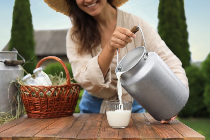 Vrouw giet melk over vanuit een kan in een glas. 