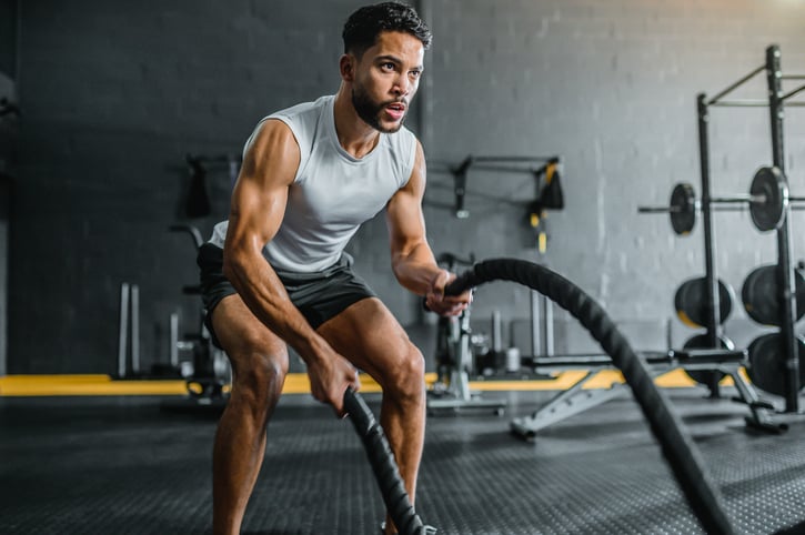 Man voert intensieve training uit met battle ropes in een moderne sportschoolomgeving, gefocust op kracht en uithoudingsvermogen