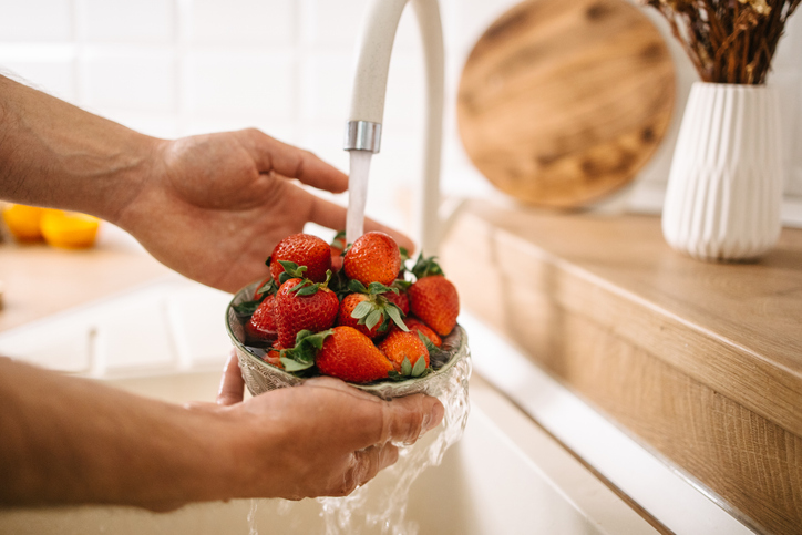 Iemand wast een kom aardbeien onder een stromende kraan in de keuken.